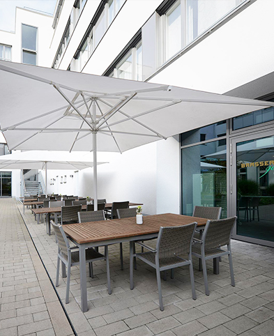 Außenbereich der Brasserie904 im Innenhof des EVK Mettmann mit mehreren Sitzgruppen und Sonnenschirmen.