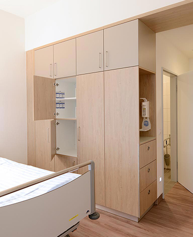 Modernes Patientenzimmer auf der geriatrischen Station des EVK Mettmann – Blick auf Bett, Schrankwand und Zimmereingang.