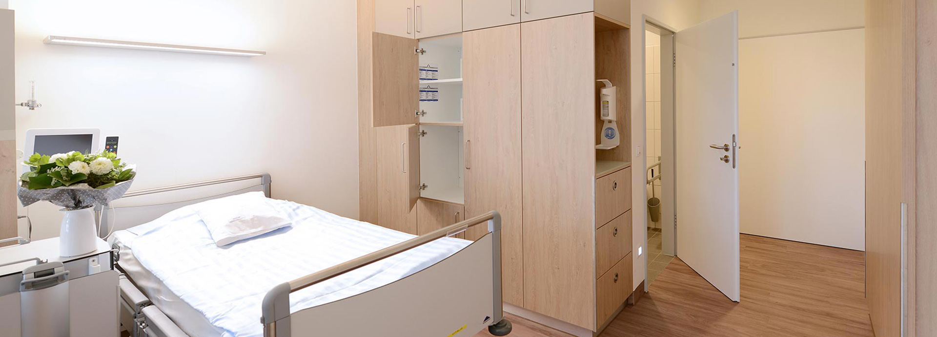 Modernes Patientenzimmer auf der geriatrischen Station des EVK Mettmann – Blick auf Bett, Schrankwand und Zimmereingang.