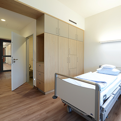 Blick in Patientenzimmer der Palliativstation mit Schrankwand in Holzoptik und modernem Patientenbett.