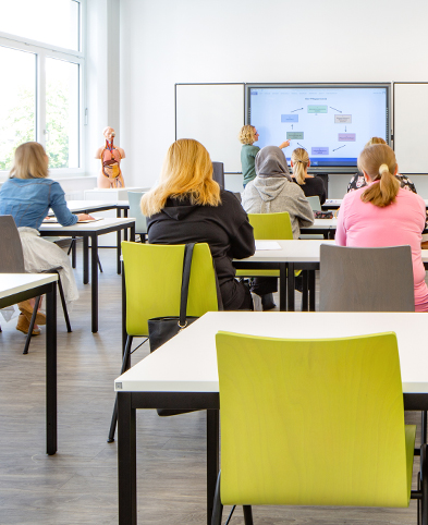 Lehrerin erklärt Auszubildenden etwas an einer digitalen Tafel im Klassenzimmer der Pflegeakademie.