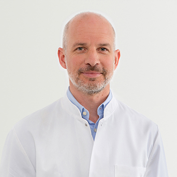 Porträtbild von Dr. med. Oliver Hofer – Chefarzt und Ärztlicher Direktor des EVK Mettmann auf grauem Hintergrund.
