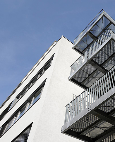 Zu sehen ist ein Teil der Fassade des EVK Mettmann mit einem Treppenaufgang. Der Blick ist von unten in Richtung blauem Himmel gerichtet.