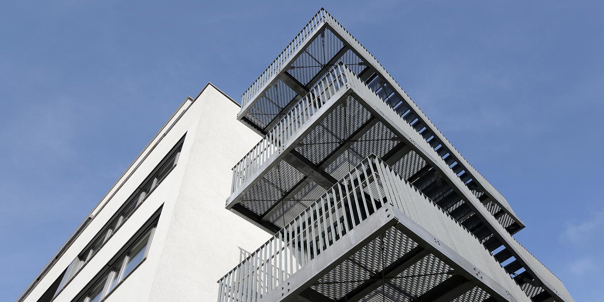 Zu sehen ist ein Teil der Fassade des EVK Mettmann mit einem Treppenaufgang. Der Blick ist von unten in Richtung blauem Himmel gerichtet.